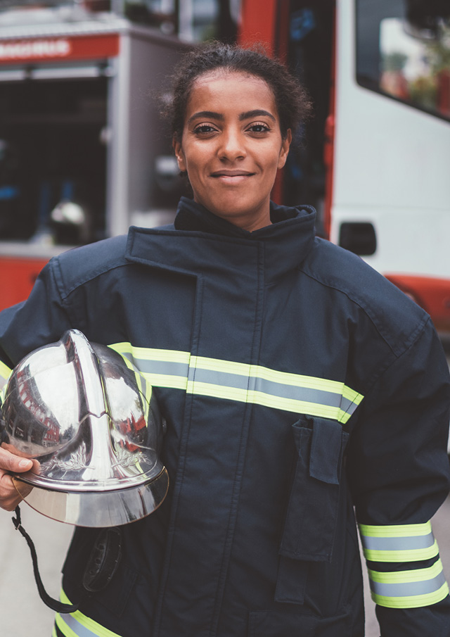 Firefighter smiling and standing in front of a fire engine holding a helmet. 