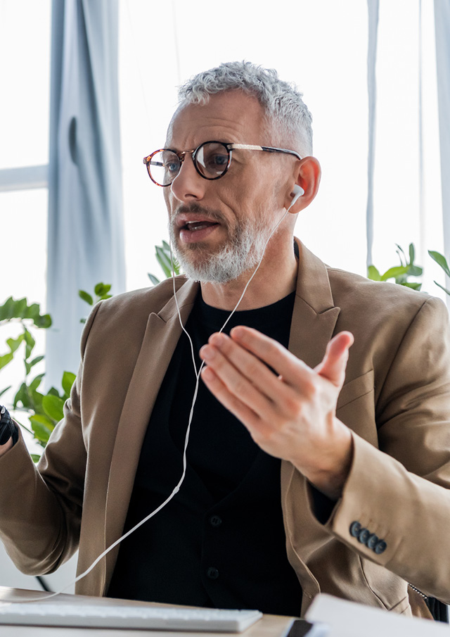 Man of middle age wearing a beige jacket and black t-shirt on a phone call using earphones.