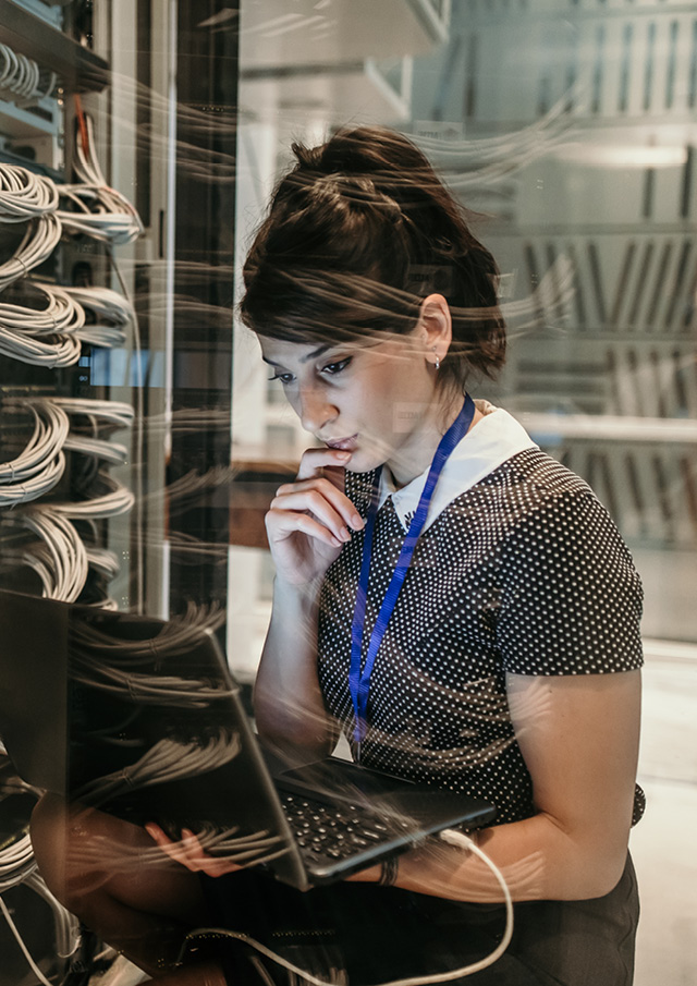 Woman sitting down and holding laptop in one hand looking at the laptop screen.